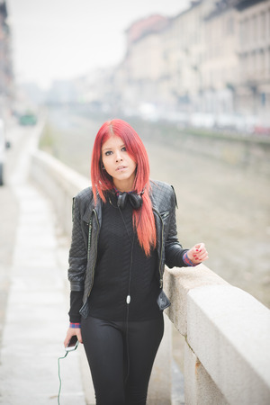 young beautiful red hair venezuelan woman lifestyle in the city of milan outdoor street listening music with headphonesの写真素材