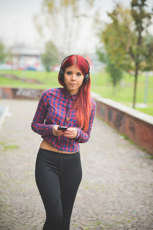 young beautiful red hair venezuelan woman lifestyle in the city of milan outdoor street listening music with headphonesの写真素材