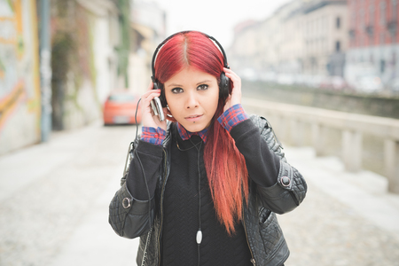 young beautiful red hair venezuelan woman lifestyle in the city of milan outdoor street listening music with headphonesの写真素材