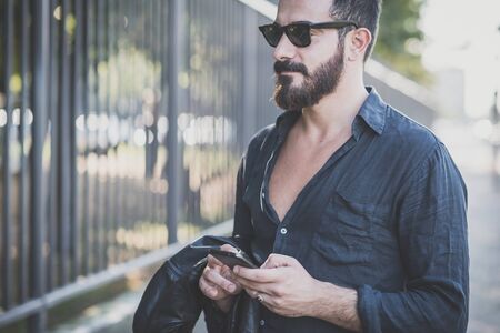young handsome attractive bearded model man using smartphone in urban contextの写真素材