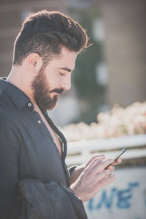 young handsome attractive bearded model man using smartphone in urban contextの写真素材
