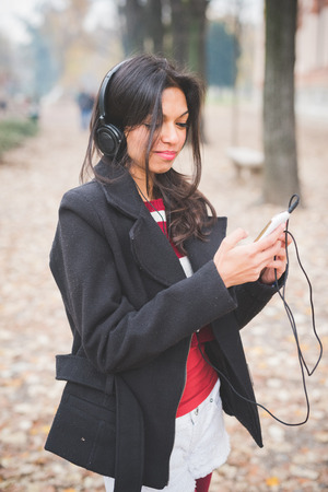 young beautiful indian woman at the park in autumn listening music with headphonesの写真素材