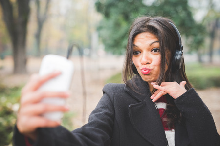 young beautiful indian woman at the park in autumn listening music with headphonesの写真素材