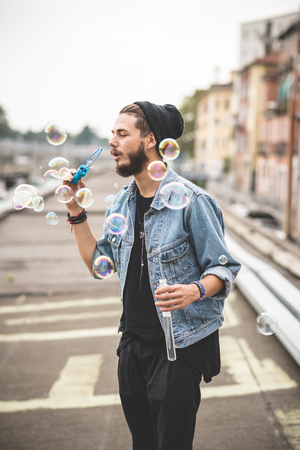 young handsome bearded hipster man blowing bubbles soap in the cityの写真素材