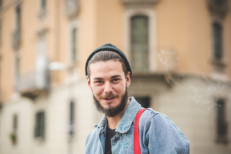 young handsome bearded hipster man smoking cigarette in the cityの写真素材