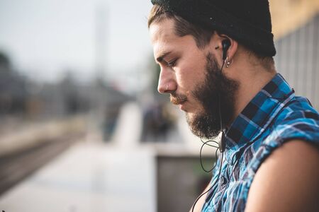young handsome bearded hipster man using smartphone and listening music with earphones in the cityの写真素材