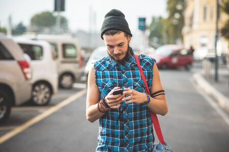 young handsome bearded hipster man using smartphone and listening music with earphones in the cityの写真素材