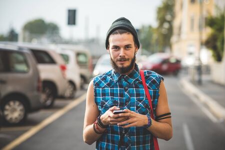 young handsome bearded hipster man using smartphone and listening music with earphones in the cityの写真素材