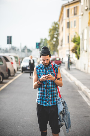 young handsome bearded hipster man using smartphone and listening music with earphones in the cityの写真素材