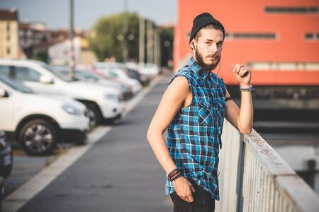 young handsome bearded hipster man using smartphone and listening music with earphones in the cityの写真素材