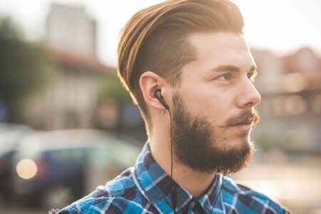 young handsome bearded hipster man using smartphone and listening music with earphones in the cityの写真素材