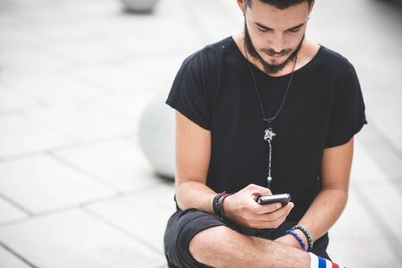 young handsome bearded hipster man using smartphone and listening music with earphones in the cityの写真素材