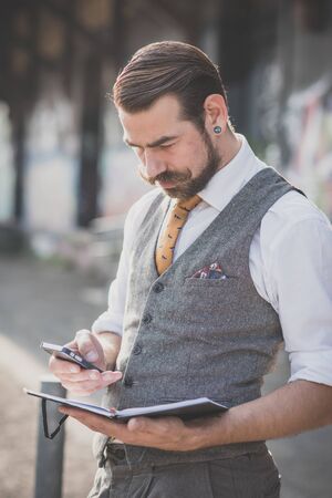 handsome big moustache hipster man with diary and smartphone in the cityの写真素材