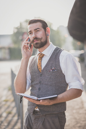 handsome big moustache hipster man with diary and smartphone in the cityの写真素材