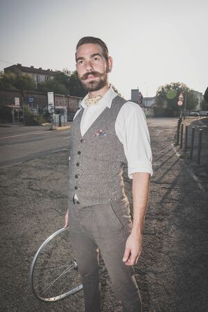 handsome big moustache hipster man holding old bicycle wheel in the cityの写真素材