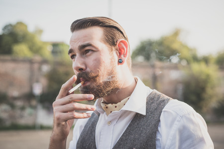 handsome big moustache hipster man smoking cigarette in the cityの写真素材