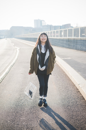 young beautiful asian hipster woman in the city - living town during sunset in backlit walking on the roadの写真素材