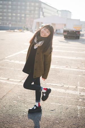 young beautiful asian hipster woman in the city - living town during sunset in backlit - smiling happyの写真素材