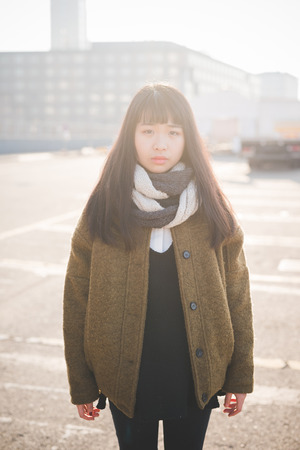 young beautiful asian hipster woman in the city - living town during sunset in backlitの写真素材