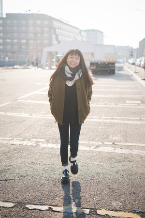 young beautiful asian hipster woman in the city - living town during sunset in backlit - smiling happyの写真素材