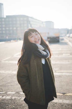 young beautiful asian hipster woman in the city - living town during sunset in backlit - smiling happyの写真素材