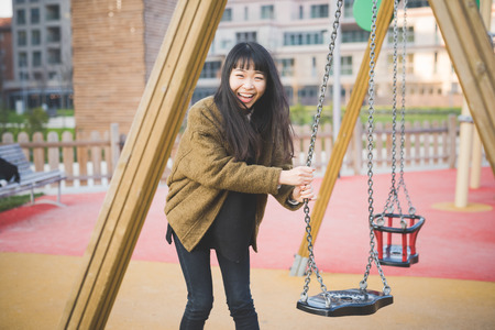 young beautiful asian hipster woman in the city - playing on a swingの写真素材