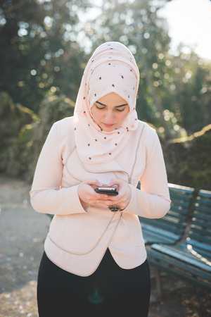 young beautiful muslim woman at the park in spring using smartphone connected online wirelessの写真素材