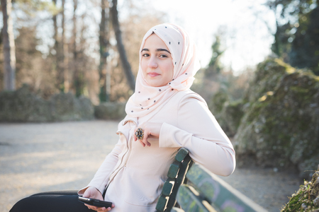 young beautiful muslim woman at the park in spring using smartphone connected online wirelessの写真素材