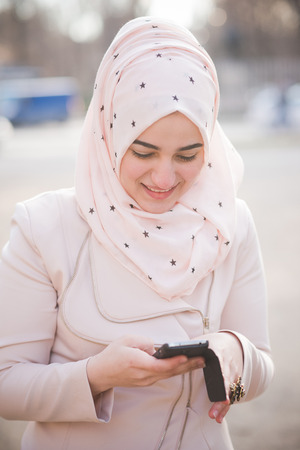 young beautiful muslim woman at the park in spring using smartphone connected online wirelessの写真素材
