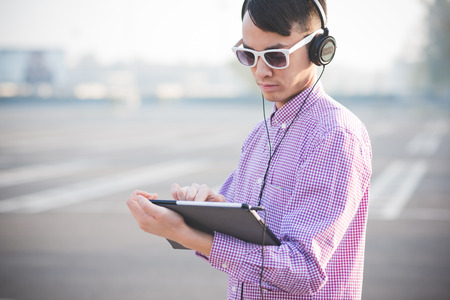 young crazy funny asian man in town outdoor lifestyle listening music with headphones and tabletの写真素材