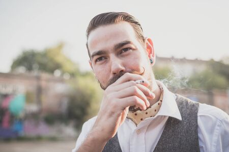 handsome big moustache hipster man smoking cigarette in the cityの写真素材