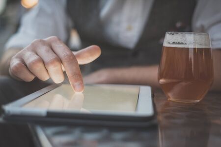 close up hand man using tablet at the bar with beer on tableの写真素材