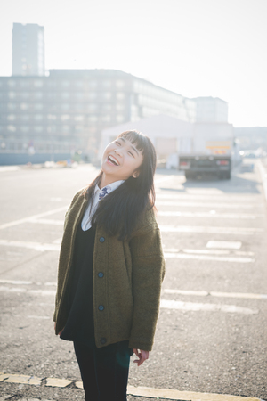 young beautiful asian hipster woman in the city - living town during sunset in backlitの写真素材