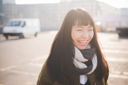 young beautiful asian hipster woman in the city - living town during sunset in backlit - smiling happyの写真素材