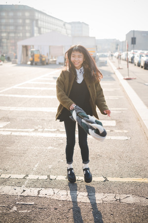 young beautiful asian hipster woman in the city - living town during sunset in backlit - smiling happy having fun with scarfの写真素材