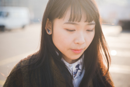 young beautiful asian hipster woman in the city - living town during sunset in backlitの写真素材