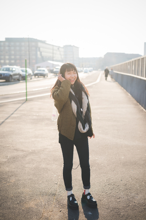 young beautiful asian hipster woman in the city - living town during sunset in backlitの写真素材