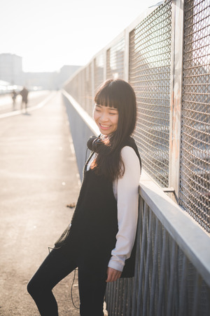 young beautiful asian hipster woman in the city - living town during sunset in backlitの写真素材