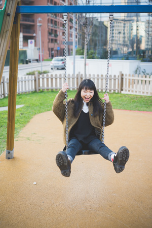 young beautiful asian hipster woman in the city - playing on a swingの写真素材