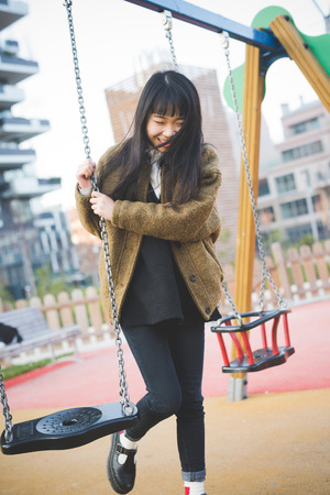 young beautiful asian hipster woman in the city - playing on a swingの写真素材