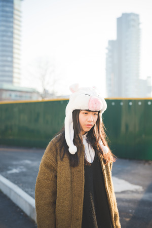 young beautiful asian hipster woman in the city - wearing funny piggy winter capの写真素材