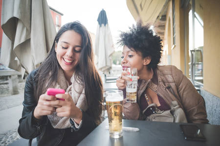 two multiethnic beautiful young woman black and caucasian using smartphone in townの写真素材