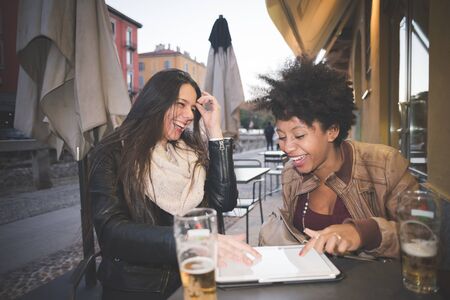 two multiethnic beautiful young woman black and caucasian using tablet in townの写真素材