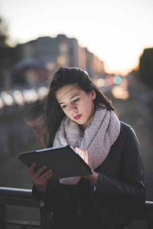 young beautiful long hair woman in town during sunset backlight using tabletの写真素材