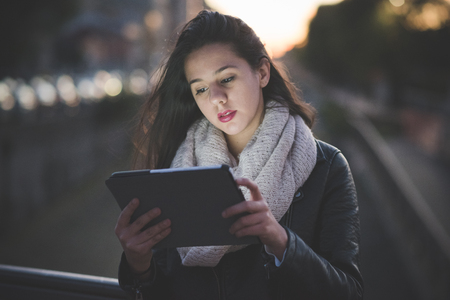 young beautiful long hair woman in town during sunset backlight using tabletの写真素材