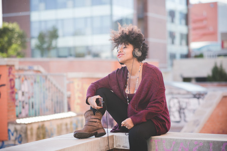 beautiful black curly hair african woman listening music with headphones in townの写真素材