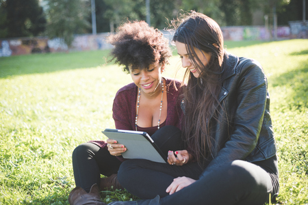 two multiethnic beautiful young woman black and caucasian using tablet in townの写真素材