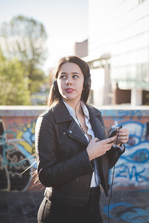 young beautiful long hair woman in town during sunset backlight listening music with headphonesの写真素材