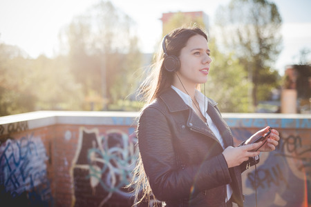 young beautiful long hair woman in town during sunset backlight listening music with headphonesの写真素材
