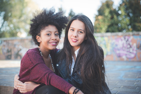 two multiethnic beautiful young woman black and caucasian having fun in townの写真素材